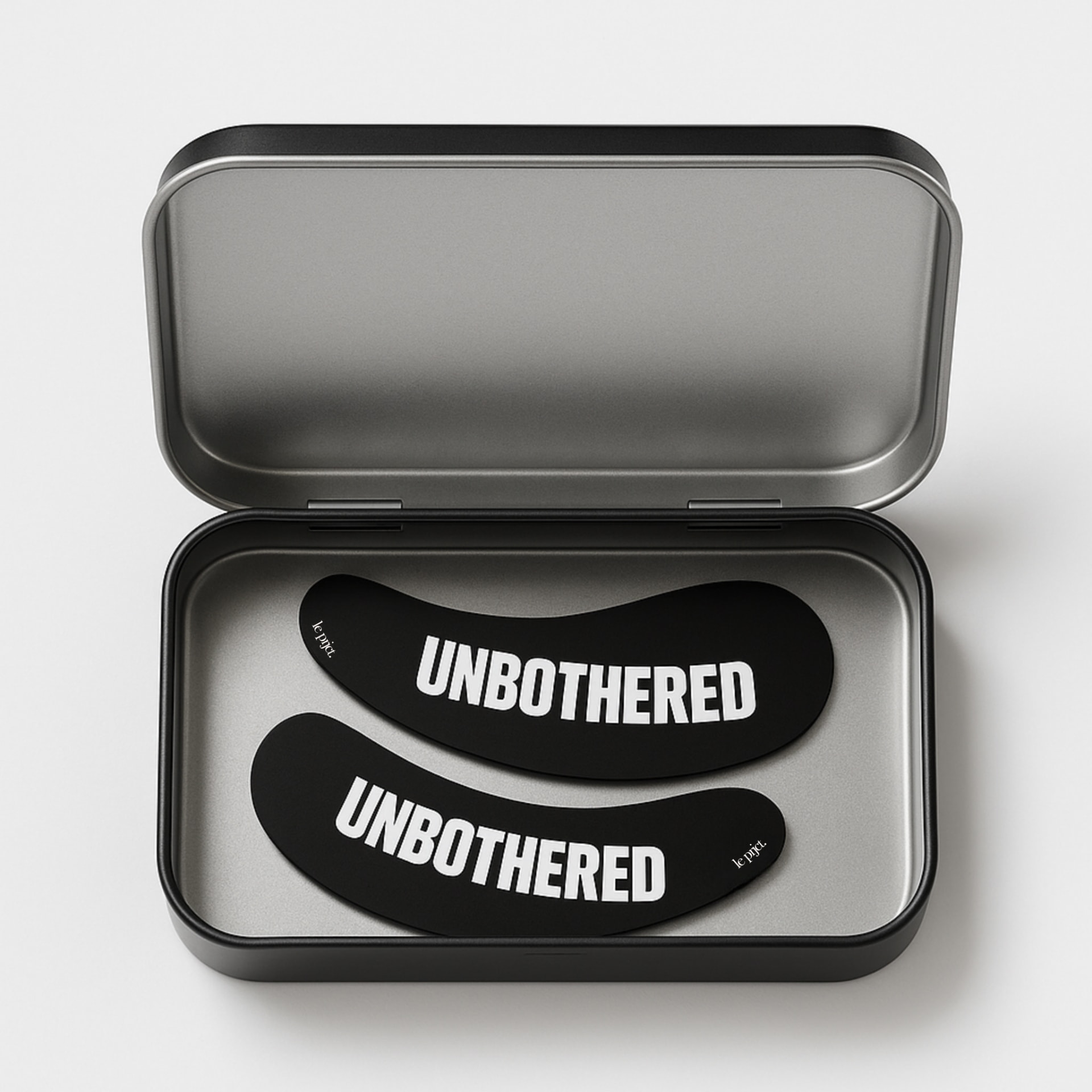 Open matte black aluminum tin holding the UNBOTHERED reusable eye masks